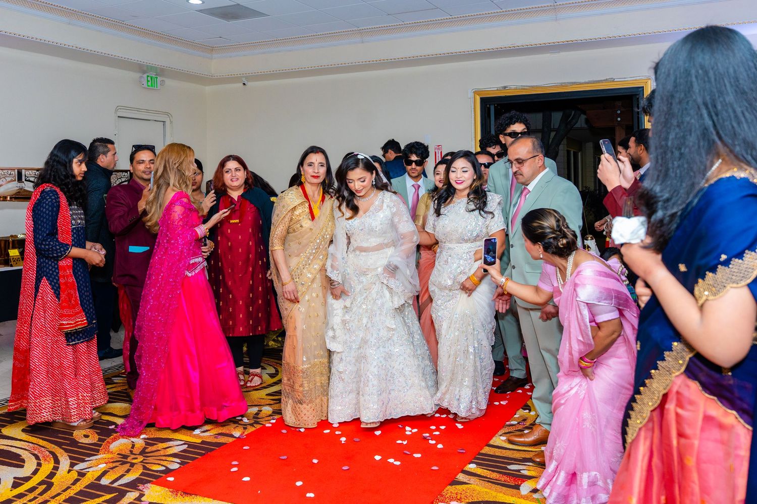 Wedding guests gathered on a red carpet in traditional South Asian formal attire.
