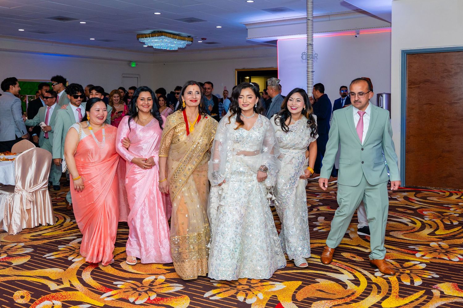 Wedding party in traditional South Asian attire posing together in an elegant ballroom.