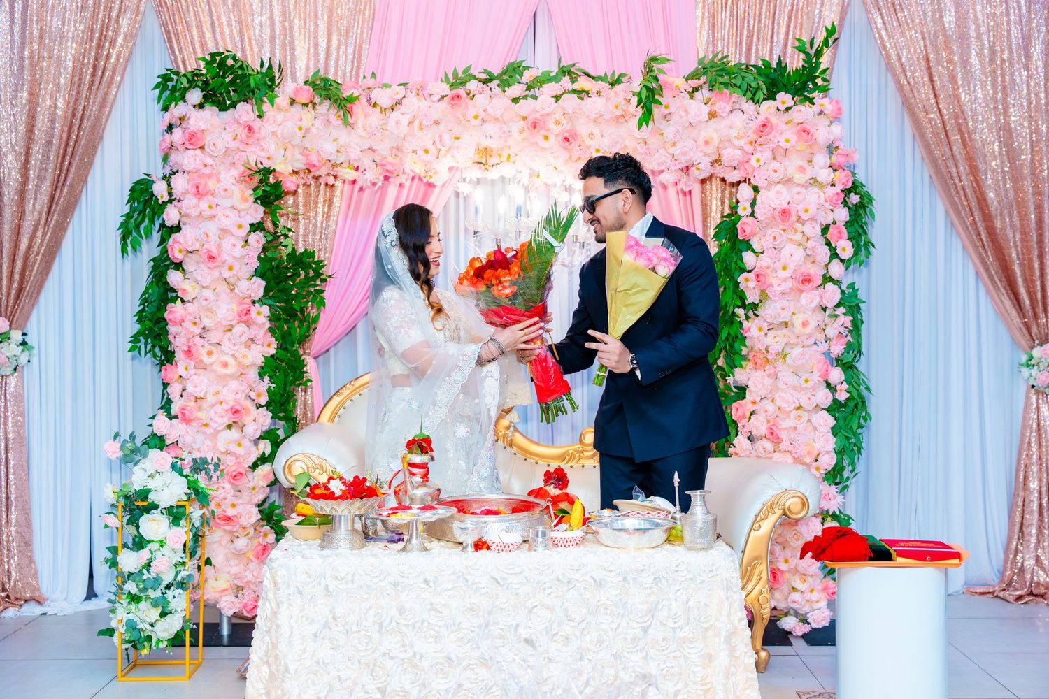 Romantic wedding scene with pink floral archway and decorated white table setting.