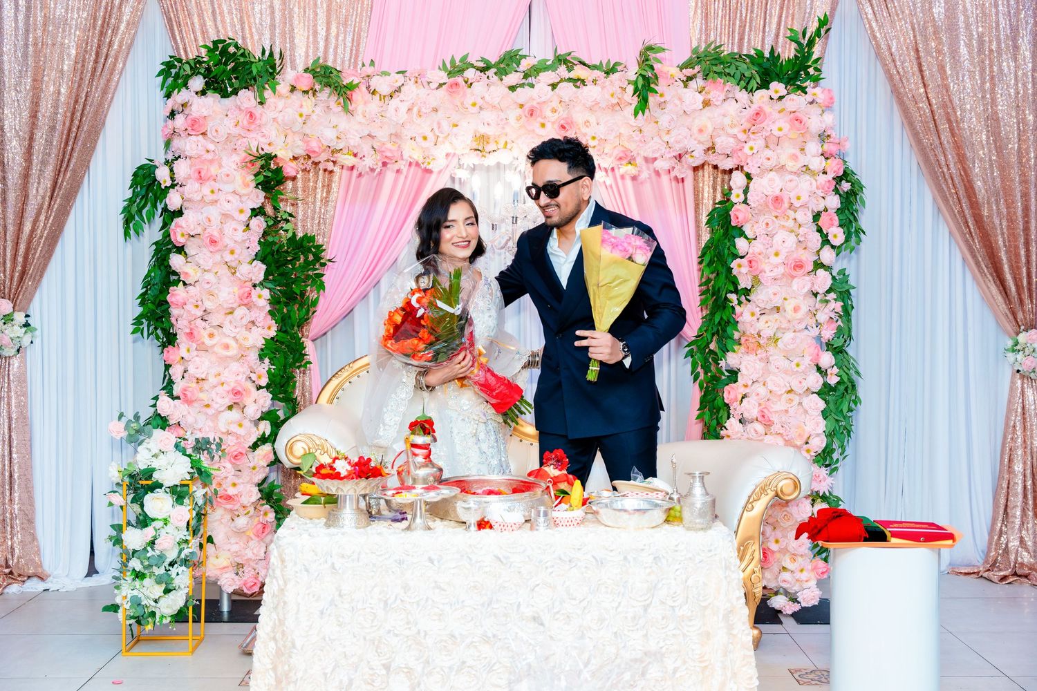 Elegant wedding setup featuring a pink floral arch and white lace-covered table.