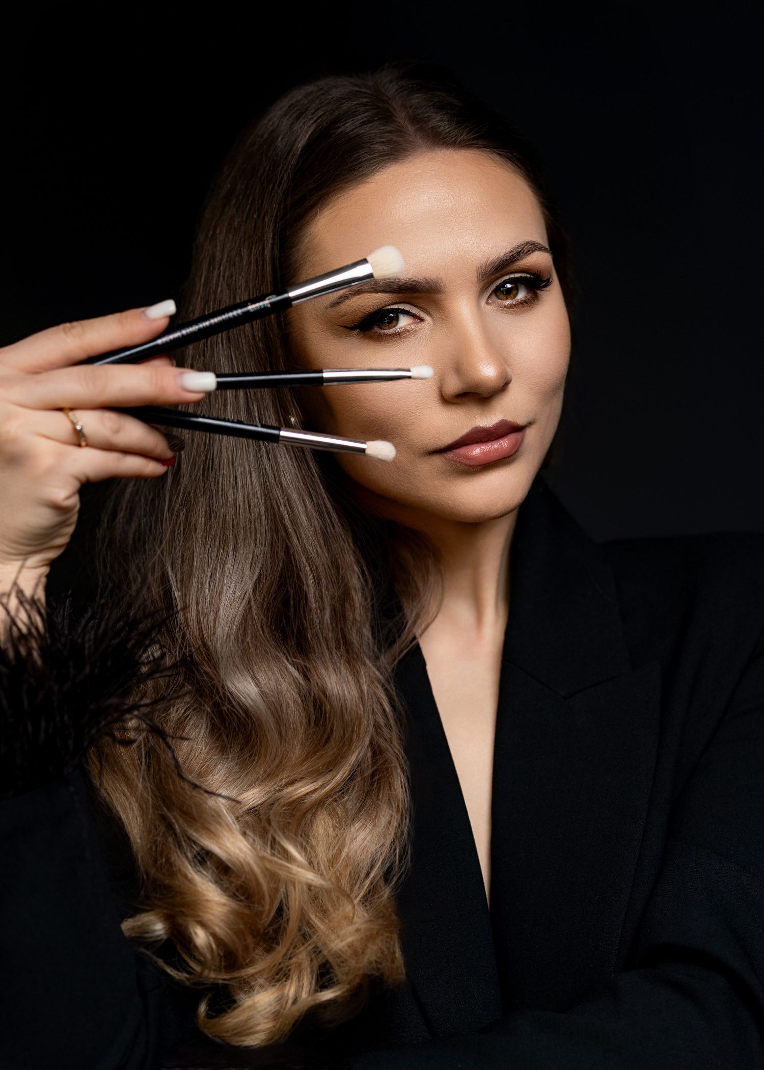 Professional beauty shot showing makeup brushes held against face on dark background.