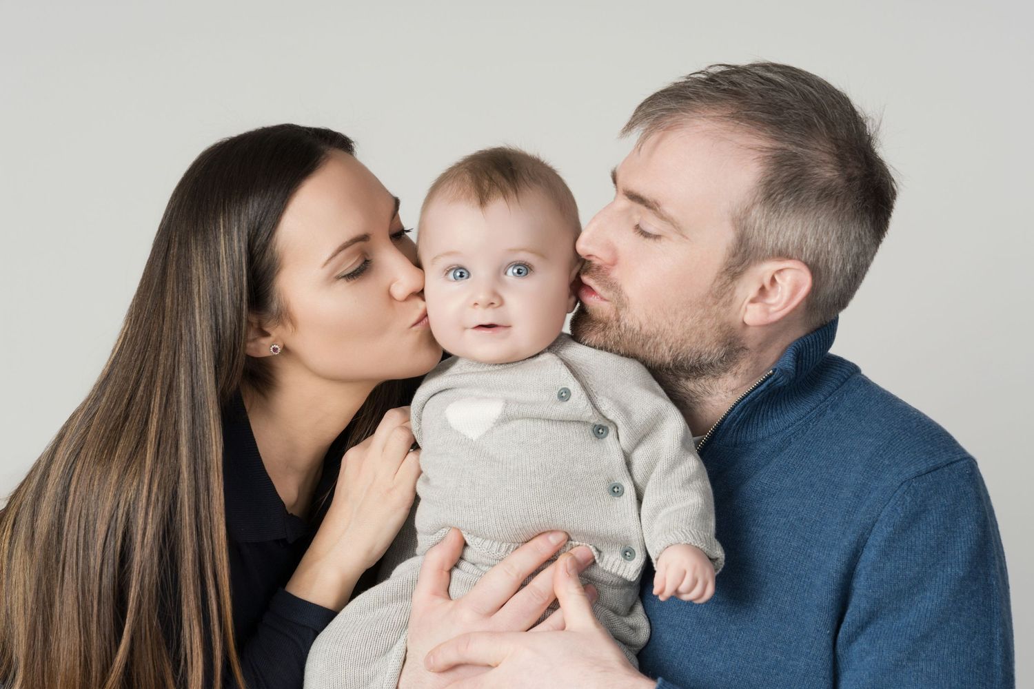 Studio portrait against grey background showing affectionate moment with baby.