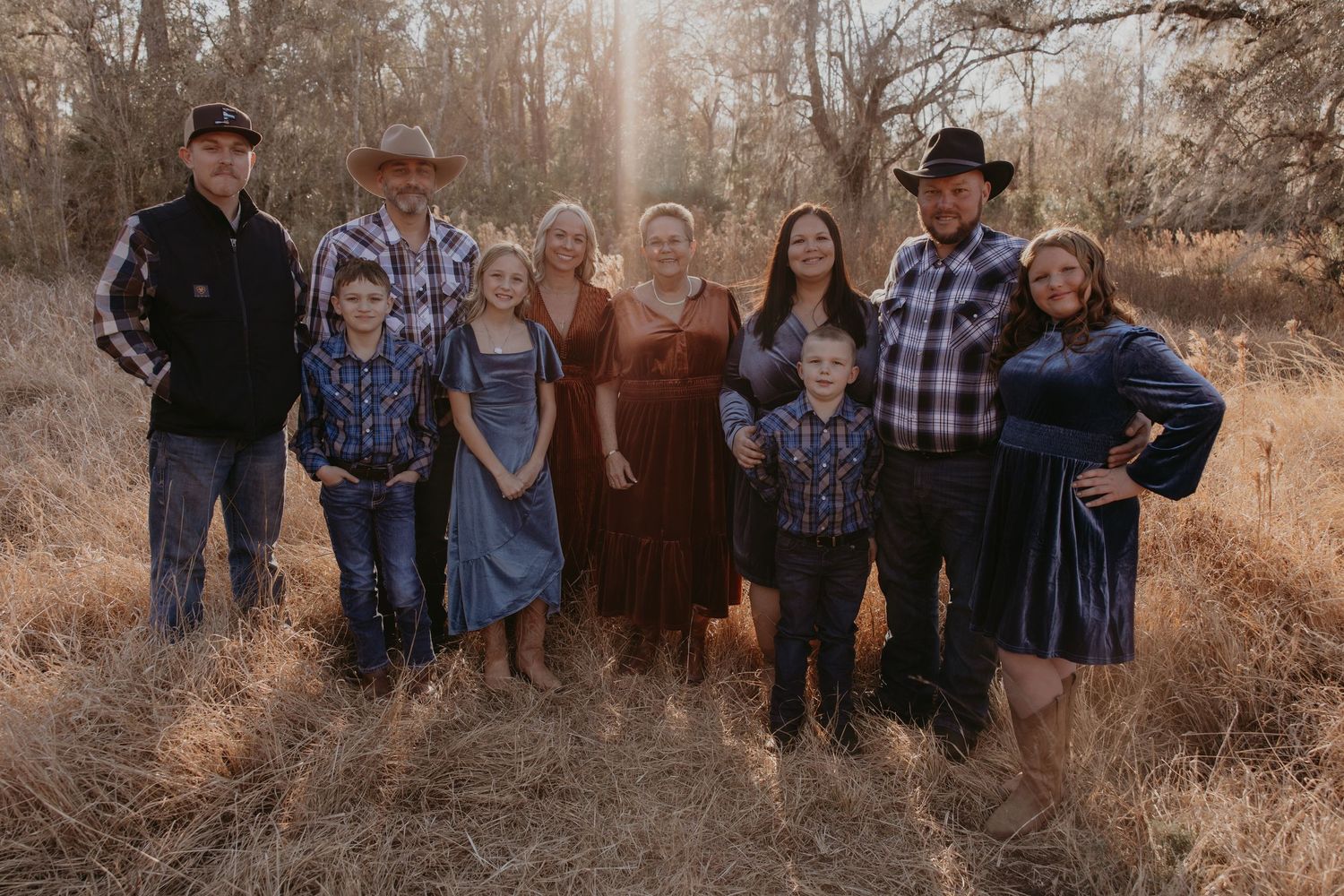 Family in flowing dresses poses together in field during golden sunset.