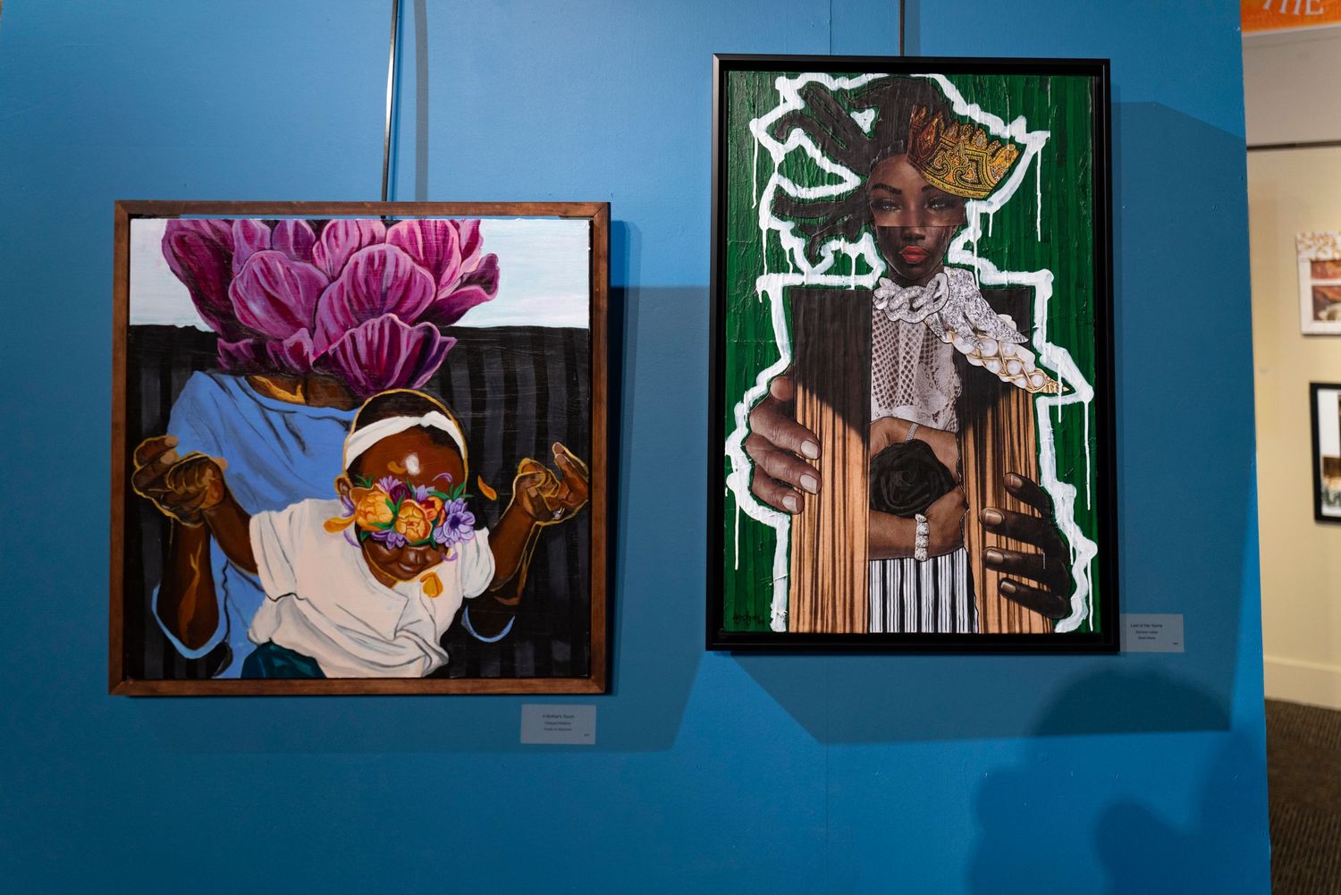 Two framed artworks on blue wall showing portraits with pink and green color schemes.
