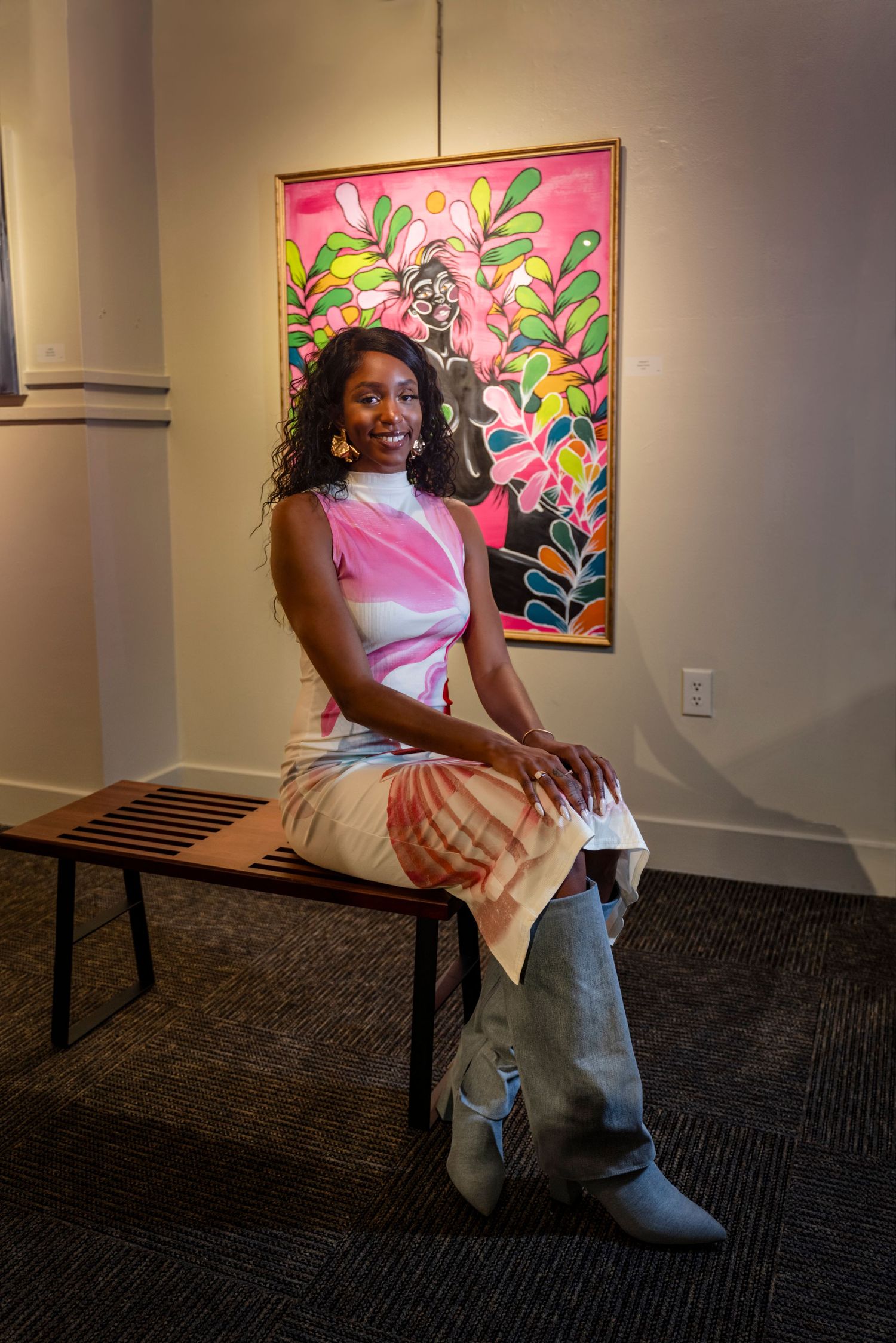 Person in pink and white outfit sits on wooden bench in front of vibrant floral artwork.