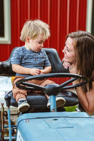 A parent and small child share a sweet moment aboard a blue tractor with red barn siding in the background.