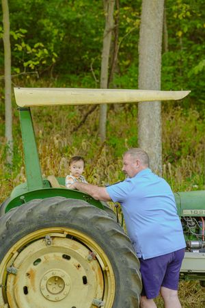 A classic green John Deere tractor parked in a wooded area during a sunny summer day.