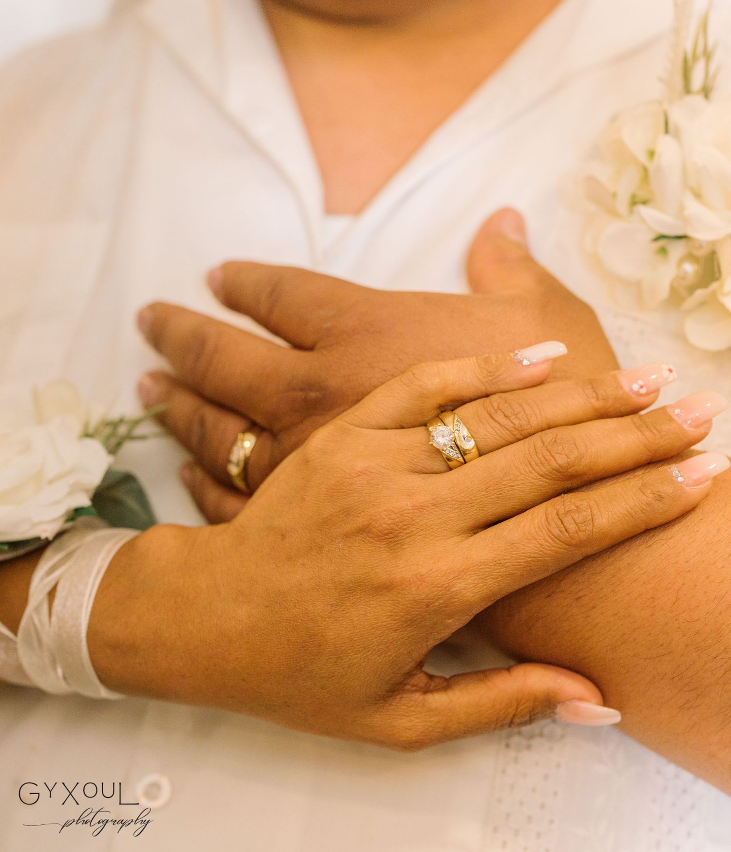 Close up of hands showing an engagement ring with white flowers in the background.