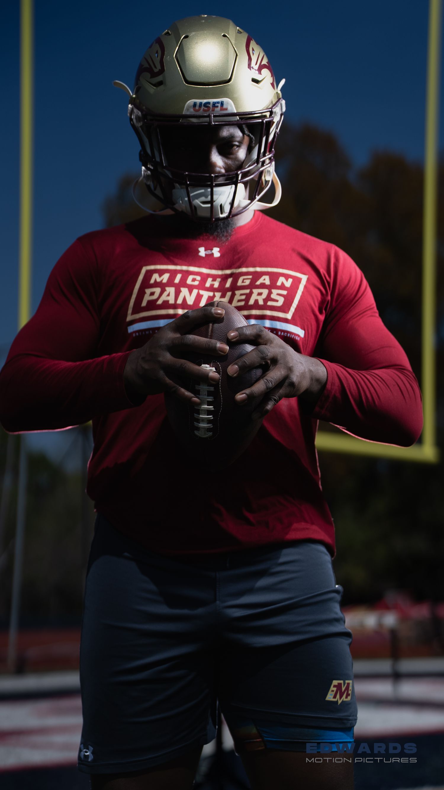 Football player wearing Michigan Panthers Under Armour gear and helmet poses on practice field.
