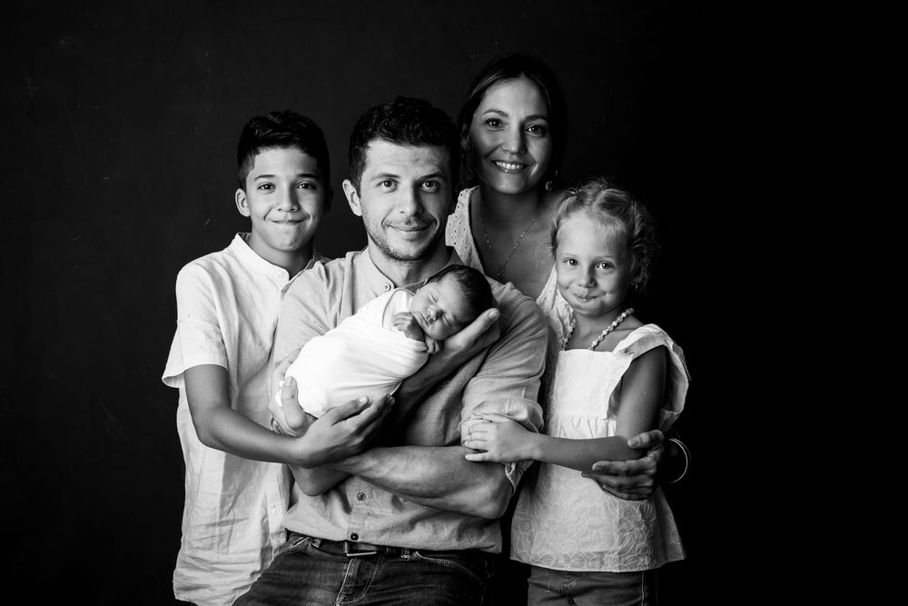 Portrait de famille en noir et blanc montrant quatre frères et sœurs et un parent dans une étreinte amoureuse sur fond sombre