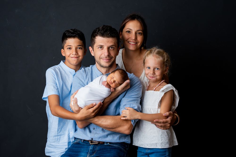 Portrait de famille avec quatre enfants et un parent vêtu de bleu et de blanc sur fond sombre.