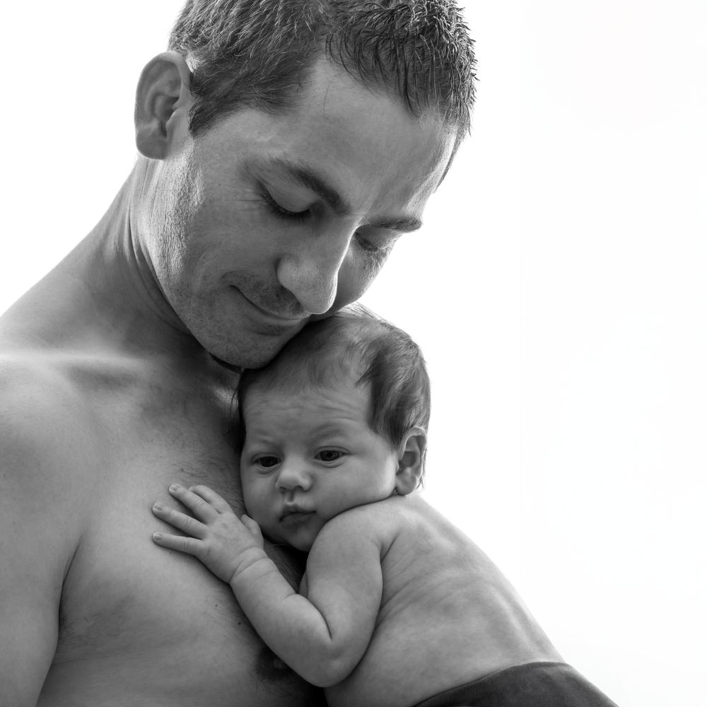 Séance Photo Portrait en noir et blanc d'un parent tenant un nouveau-né endormi contre sa poitrine nue dans un moment de tendresse intime.