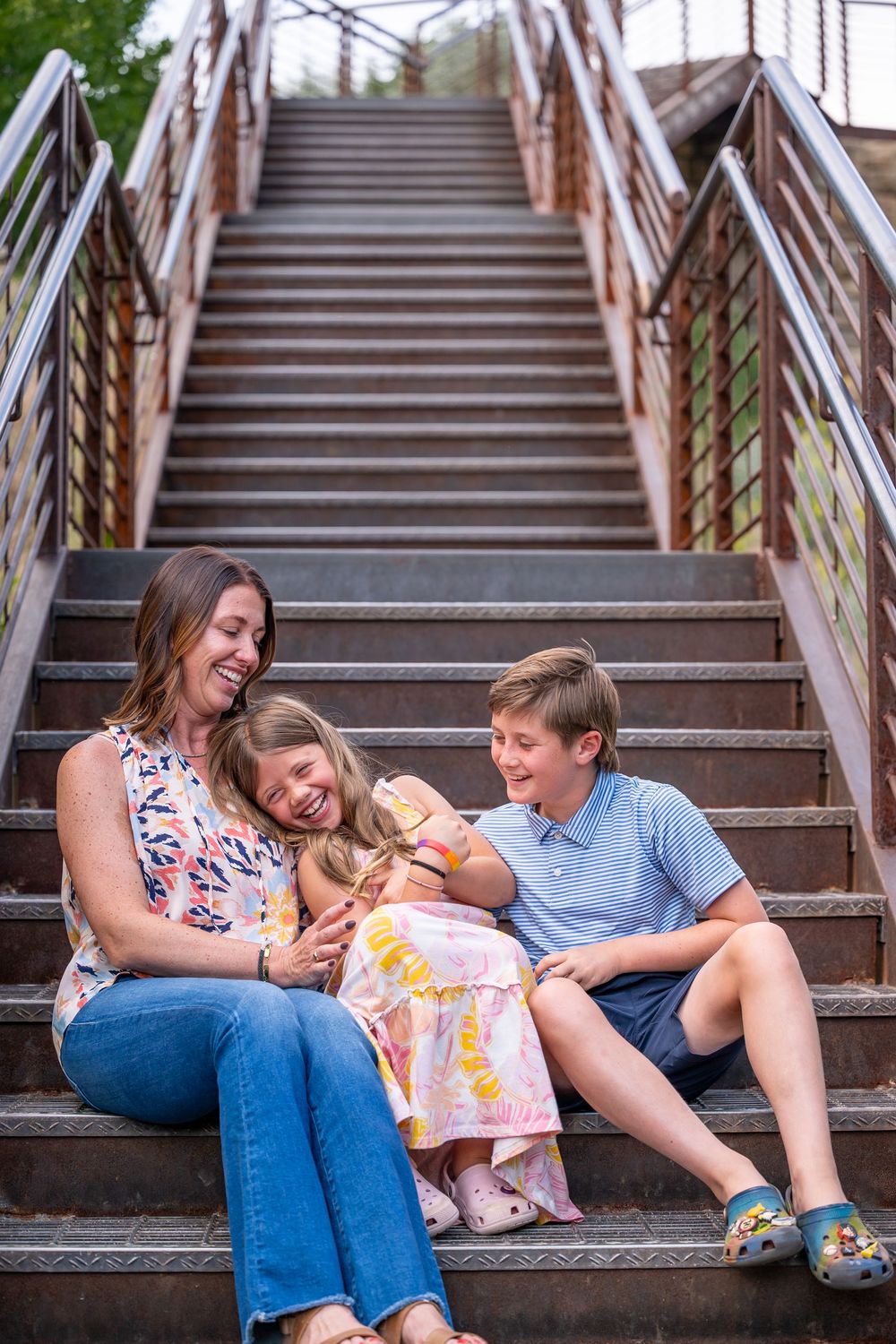 Happy family laughing and playing together while sitting on wooden stairs outdoors near trees.