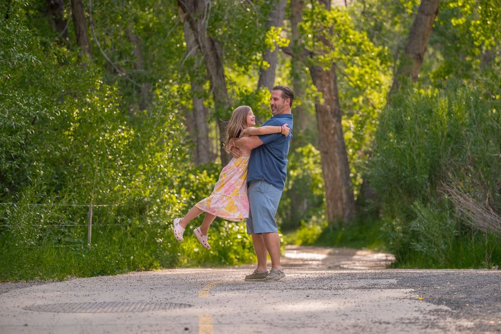 Couple dancing and spinning together on a tree-lined gravel path during a sunny summer afternoon.