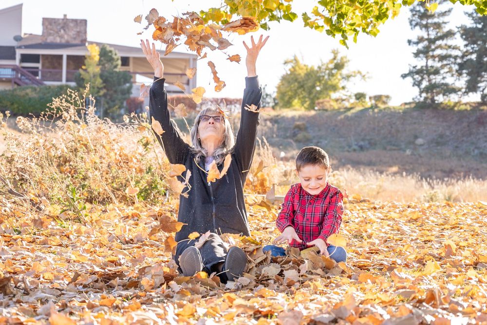 Two children play together in a pile of fallen autumn leaves on a sunny afternoon.
