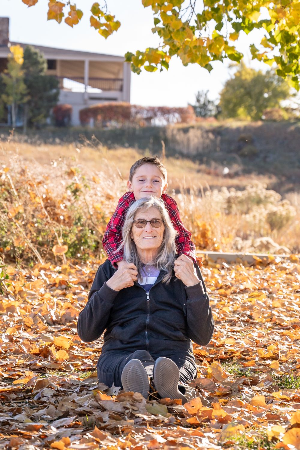 A touching autumn scene with family members sitting among fallen yellow leaves on a sunny fall day.
