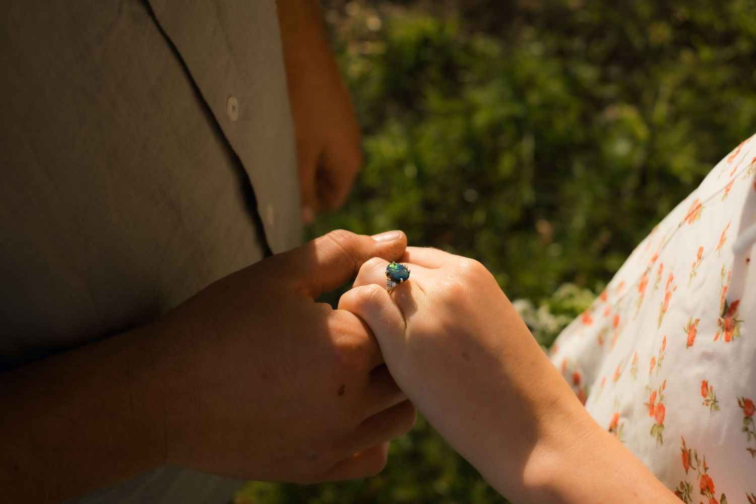 Two hands tenderly hold each other in a loving moment outdoors with greenery in the background.