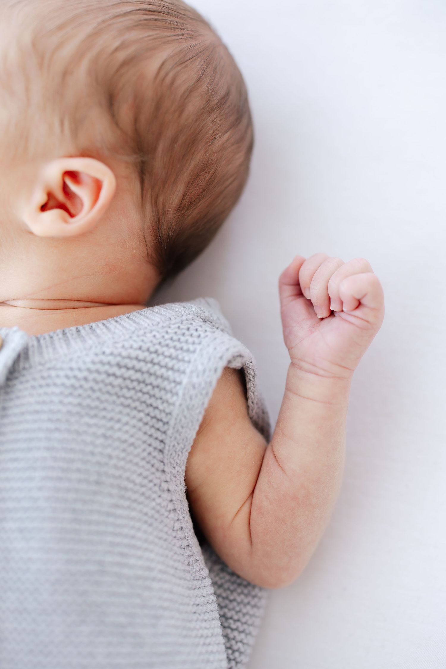 Close up of sleeping baby's ear and tiny fist against white background.