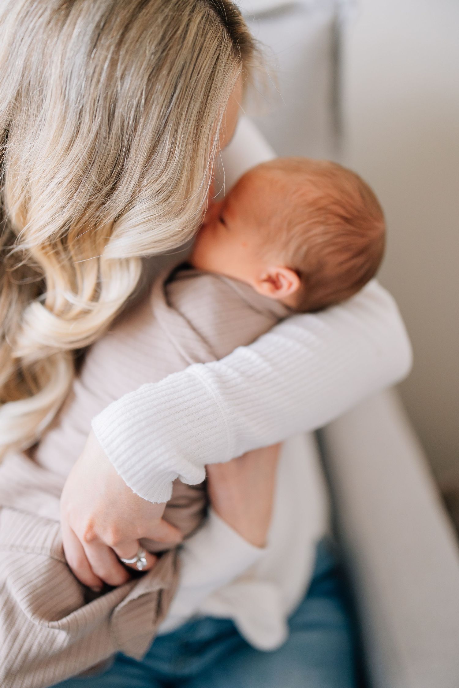 Person in white sweater cradling and embracing sleeping newborn baby.