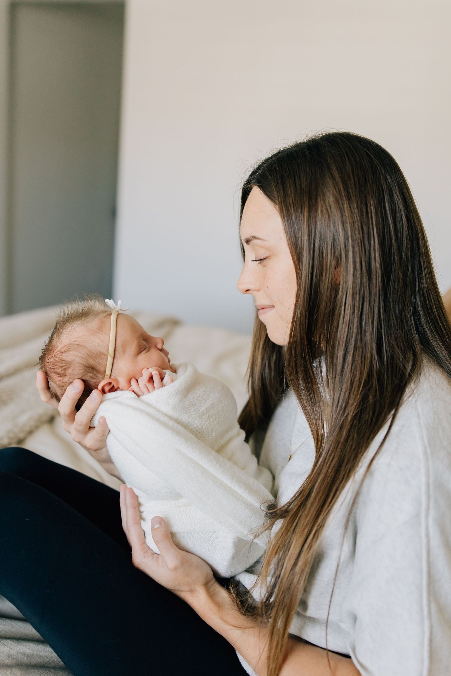 A tender moment between a woman with long dark hair holding a swaddled newborn baby.