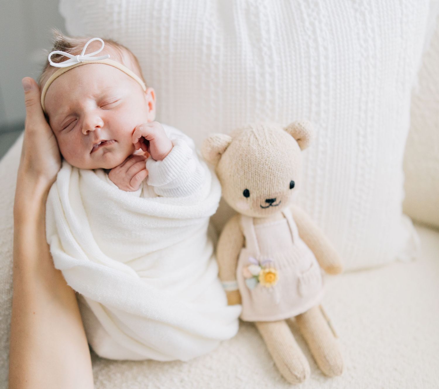 Sleeping newborn baby wrapped in white blanket next to small teddy bear.