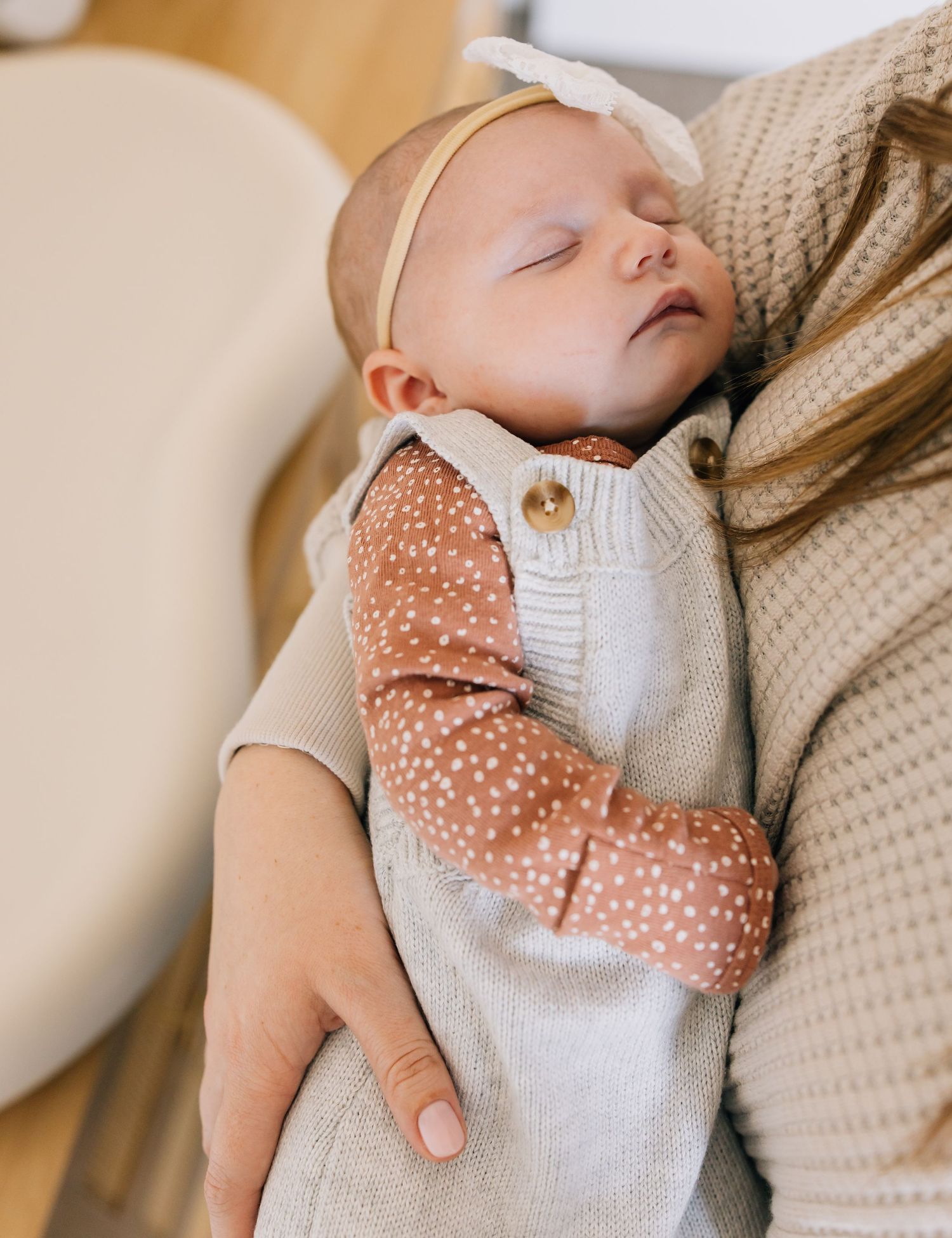 Sleeping baby in polka dot outfit wearing cream headband.
