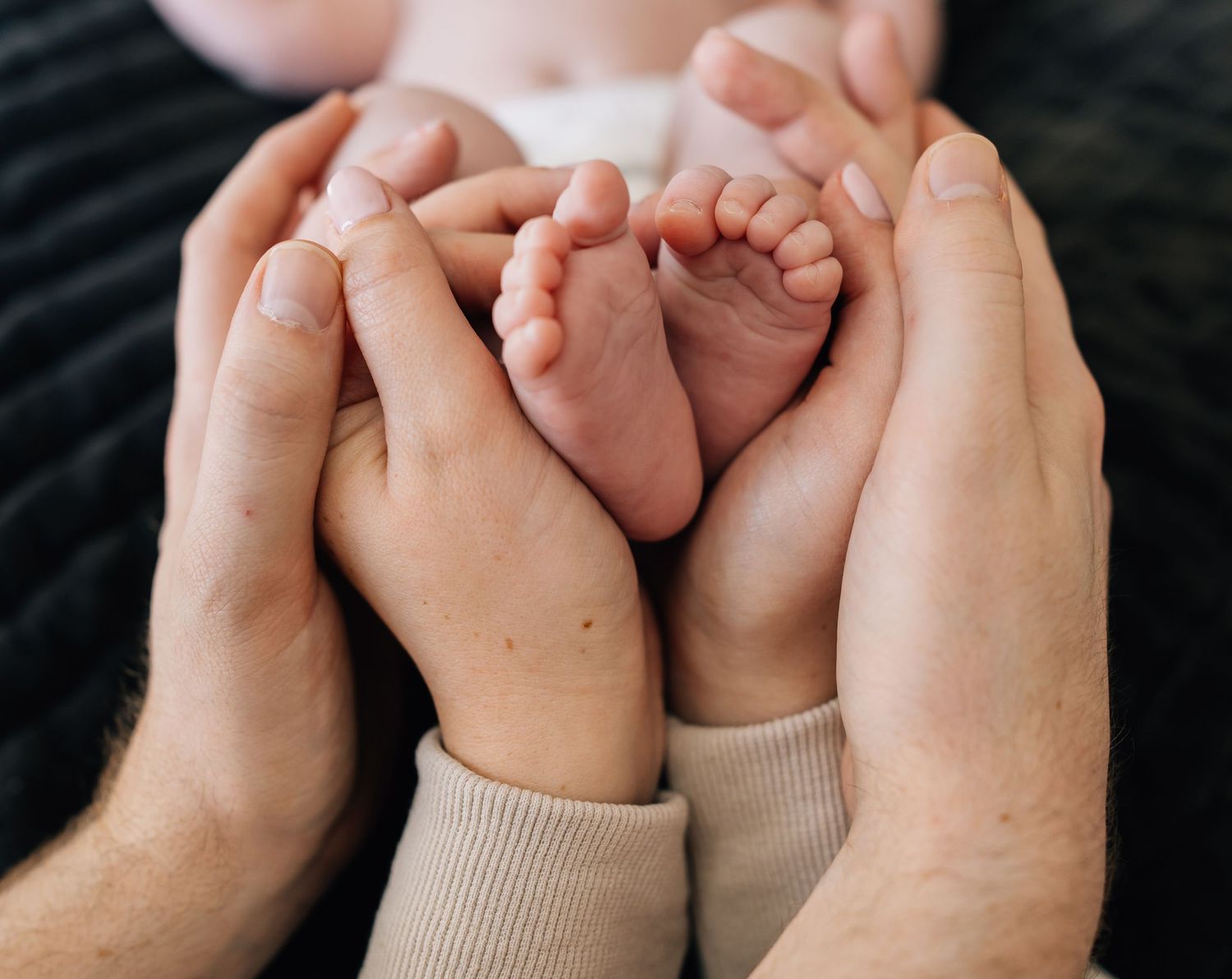 Close up of tiny newborn baby feet cradled in adult hands.