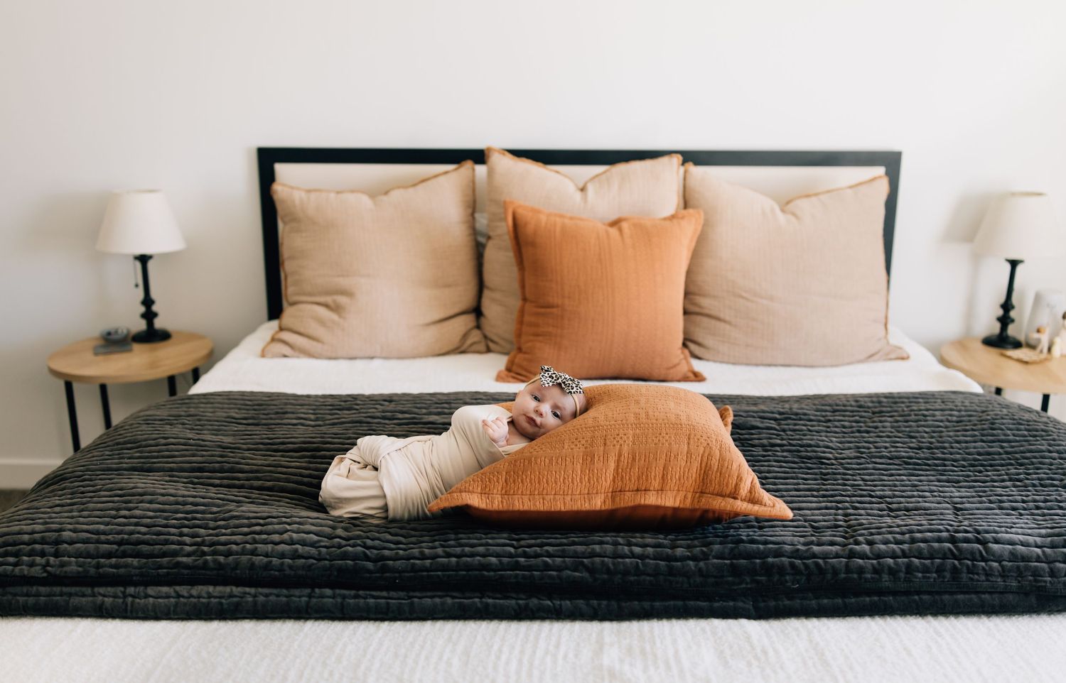 Modern bedroom with black bed frame, gray bedding and peach accent pillows.