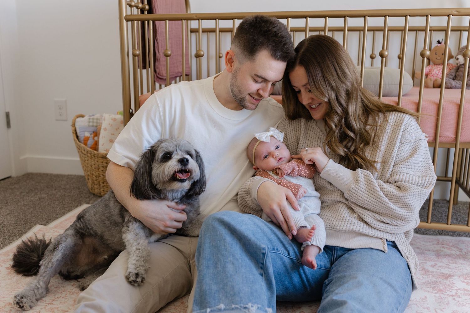 Family sitting together with their dog and newborn baby in a nursery.