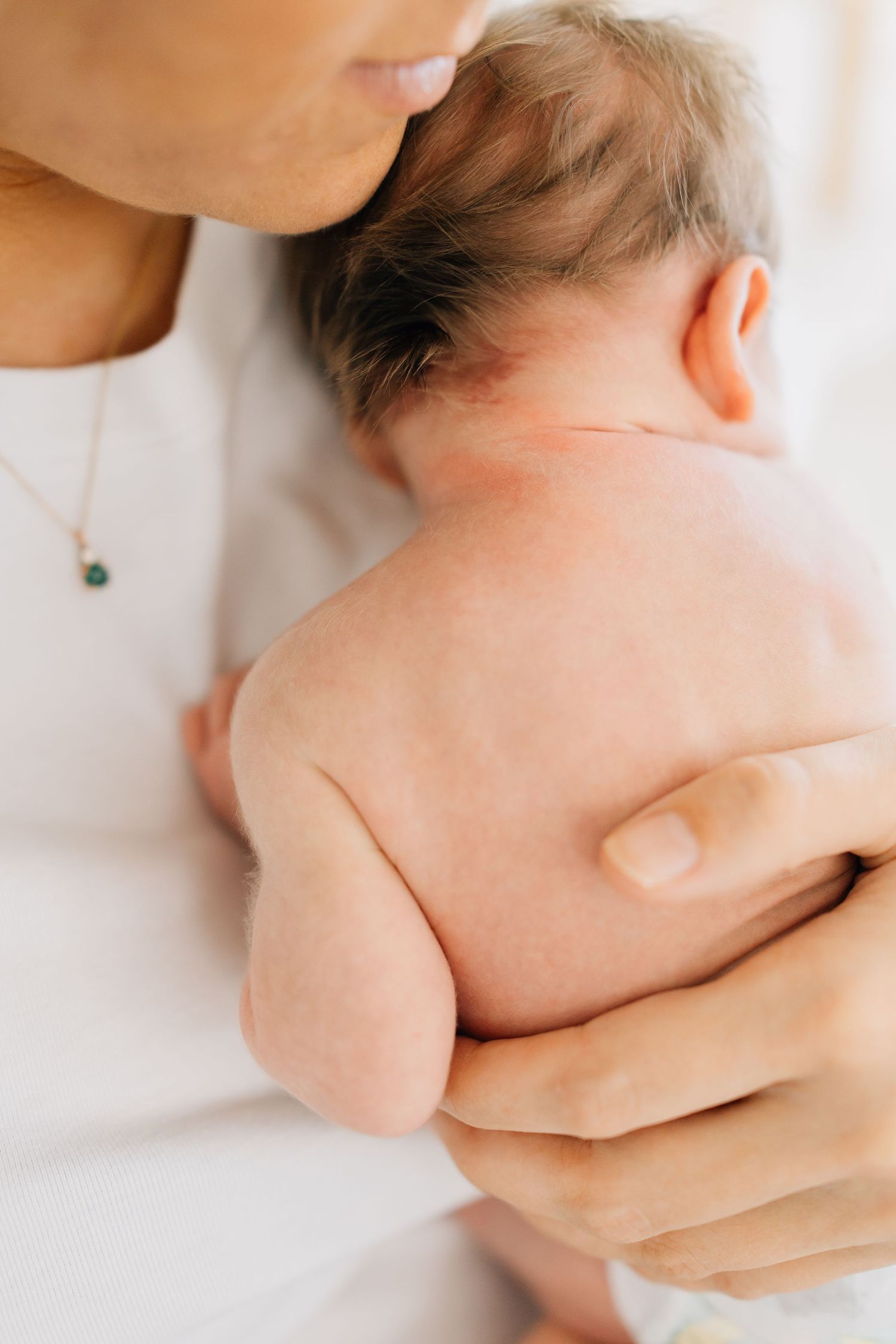 Close up of parent holding and kissing bare shoulder of infant.
