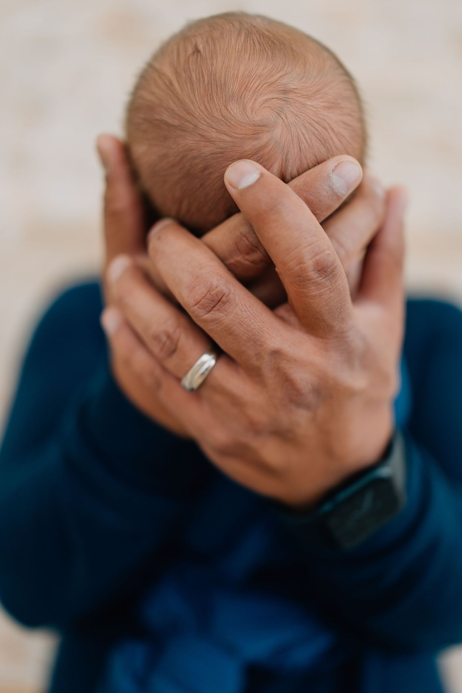 Close up of hands cradling newborn baby's head showing wedding ring.