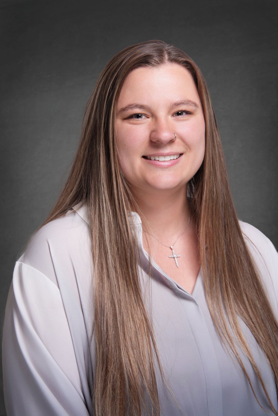 Professional headshot of a smiling woman with long straight hair wearing a white blouse and a cross necklace.