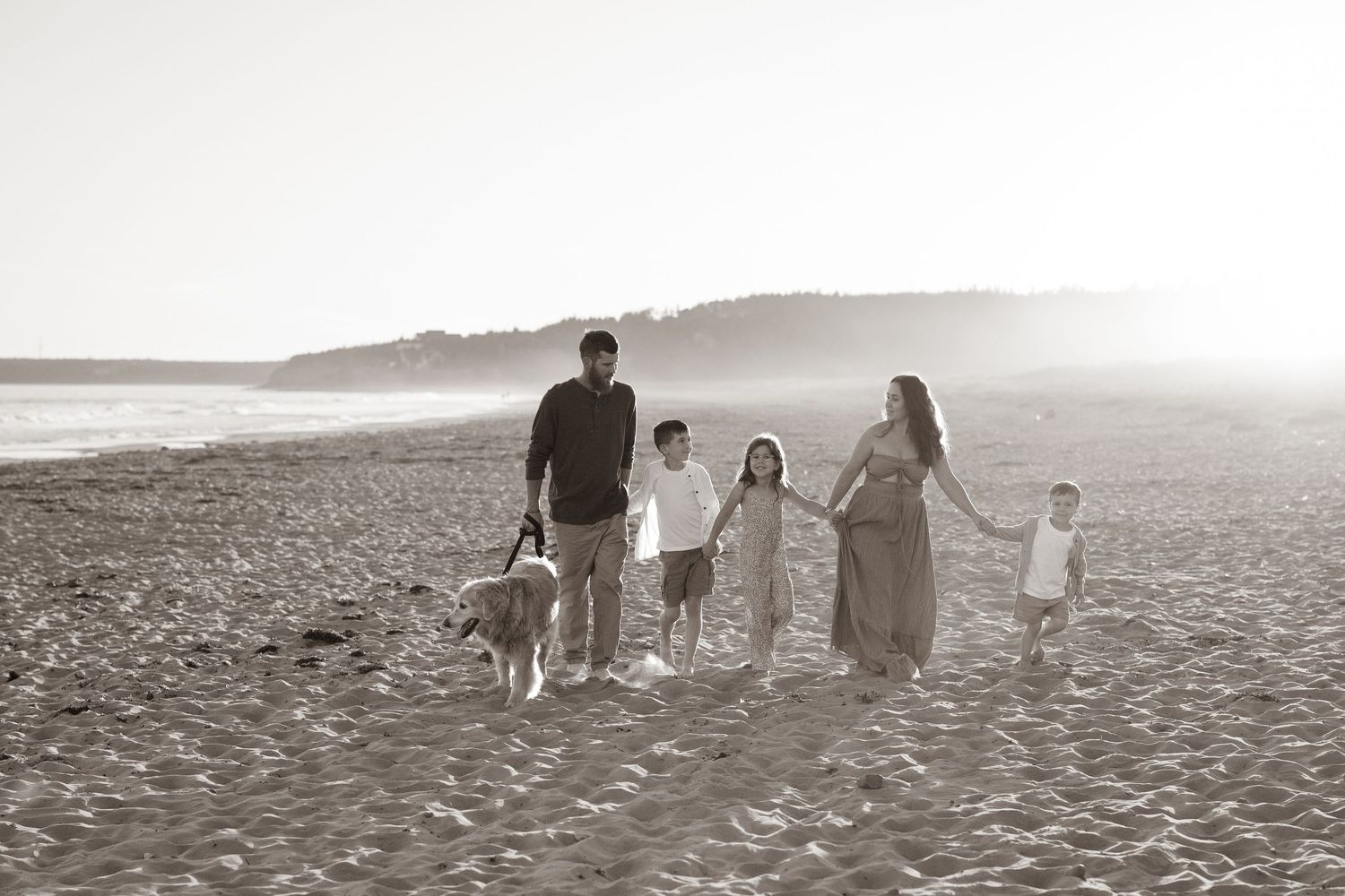 Family of five plus their golden retriever walking down the beach holding hands smiling and enjoying the sunset