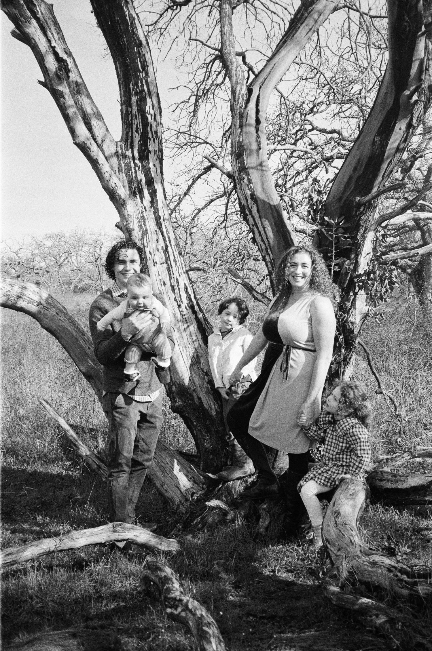 Black and white family photo of parents and children posing by a large bare tree outdoors.