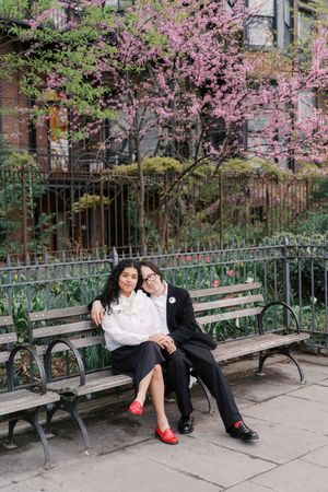 Couple sitting close together on a park bench surrounded by pink cherry blossoms in spring.