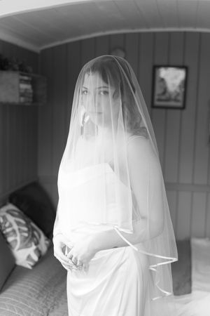 Black and white portrait of a bride in a white gown and veil, posing elegantly indoors on her wedding day.