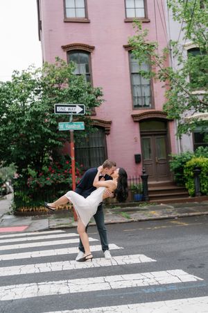 Couple shares a romantic dip kiss on a crosswalk in front of a pink building in New York City.