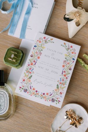 Floral wildflower wedding invitation for Yvelin Lim and Roy Jacob, May 30 2026, styled with ring, perfume, and gold accessories.