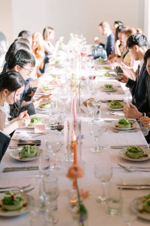 Guests dining at a long elegantly set wedding reception table with candles, glassware, and green salad plates.