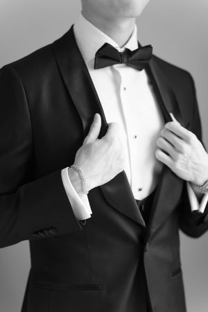 Black and white photo of a man in a tuxedo with bow tie, adjusting his jacket lapels.