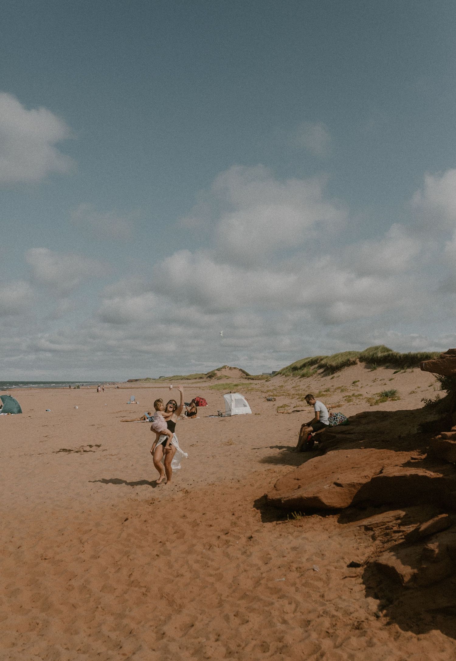 A mom says hi to her family photographer approaching the beach for their PEI family photography session at Thunder Cove Beach
