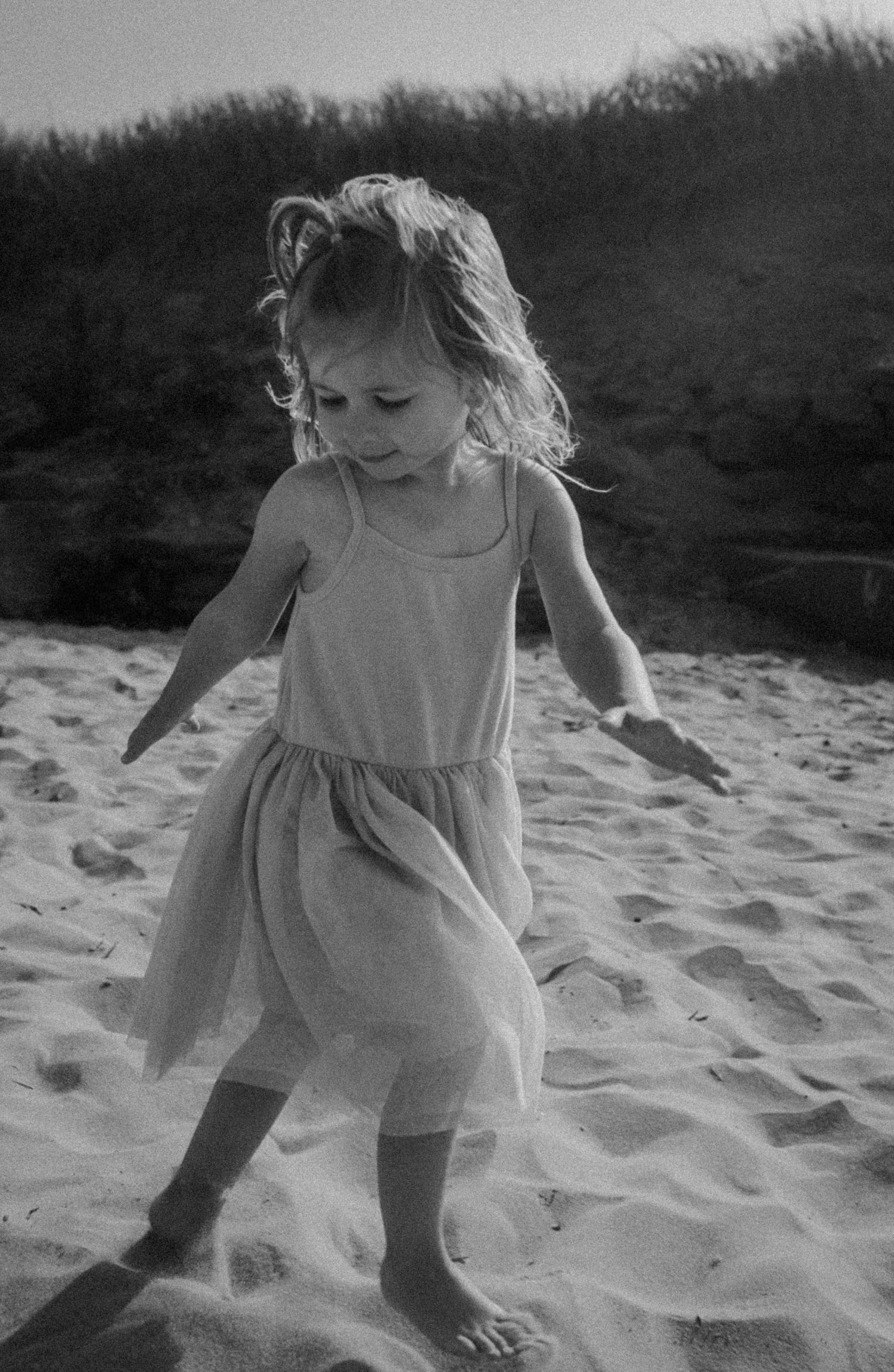 Young girl in tulle dress walking barefoot on  PEI sand dunes in black and white photo.