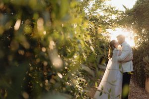 Couple sharing a romantic kiss surrounded by lush green foliage with golden sunset light filtering through the trees.