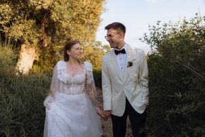 Bride and groom holding hands, walking through lush greenery, smiling at each other on their wedding day.