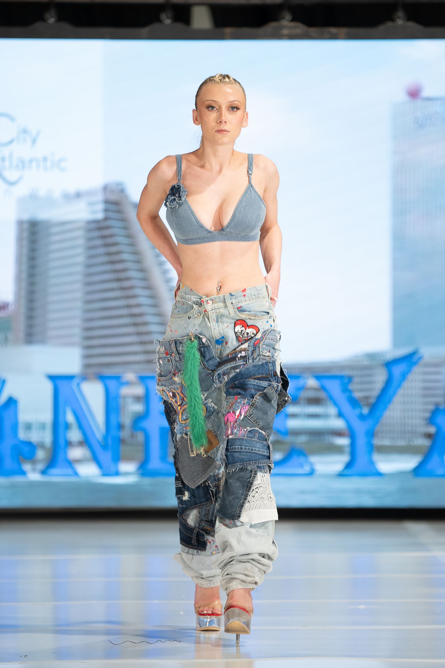 Model walks runway in denim bralette and patchwork jeans at City Atlantic fashion show.