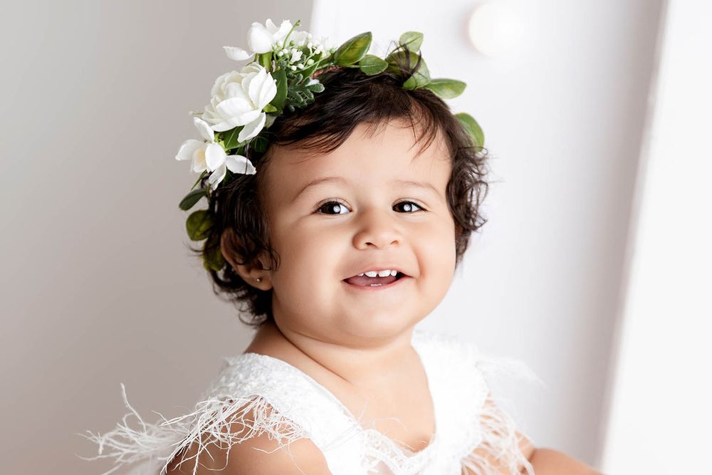Baby girl wearing a white floral crown and white feather dress poses for a first birthday portrait by Wildomar 1st birthday photographer.