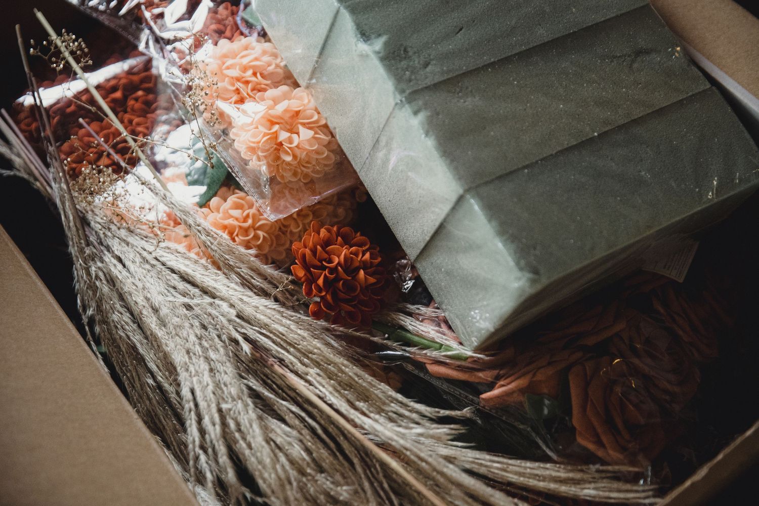 A cardboard box filled with assorted dried flowers and foliage wrapped in tissue paper for shipping.