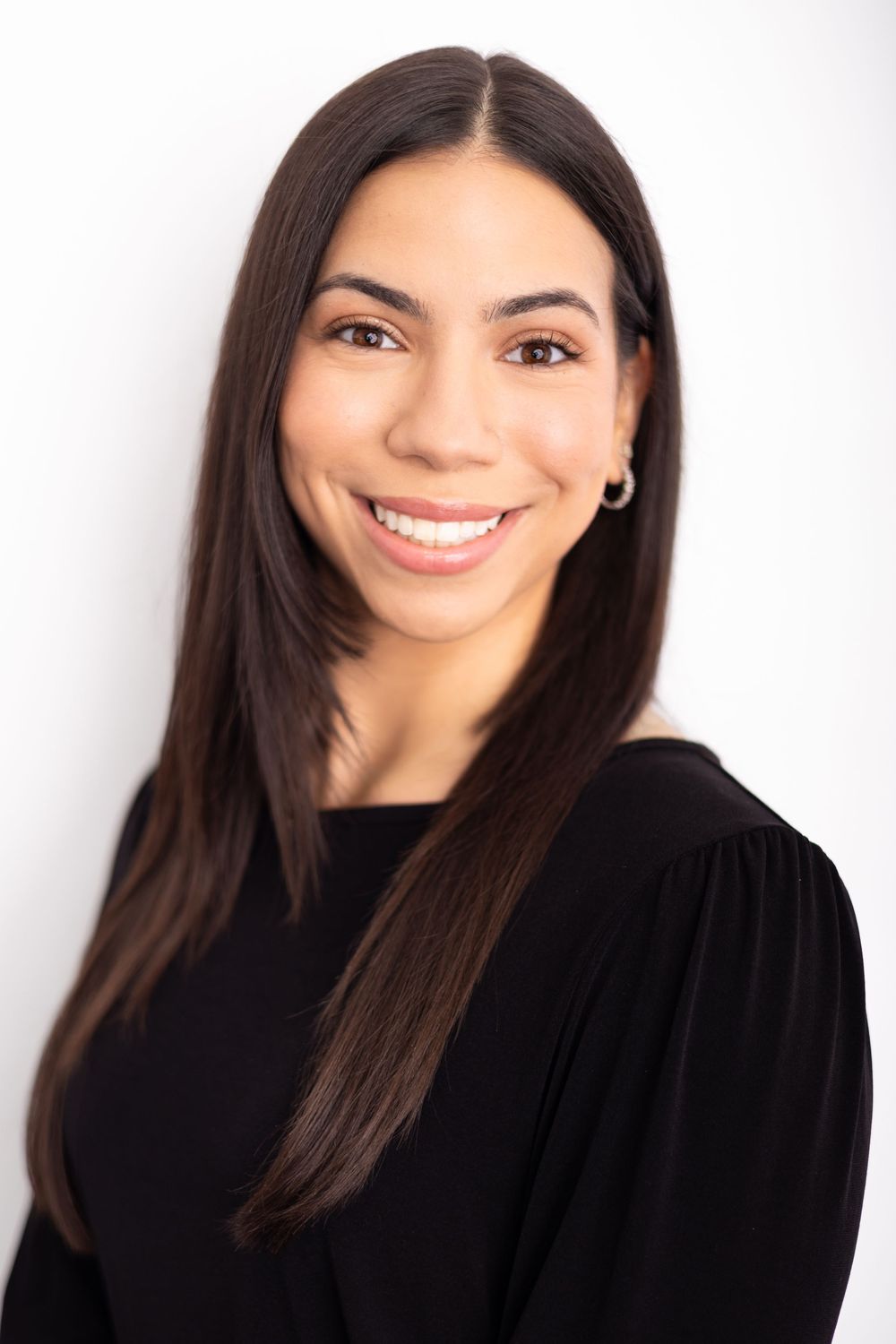 Professional headshot of a smiling young woman with long dark hair wearing a black top against a white background.