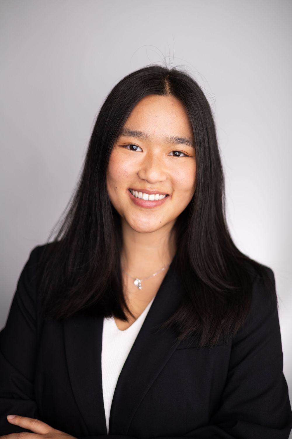 Young professional woman in black blazer smiling confidently for a corporate headshot portrait.