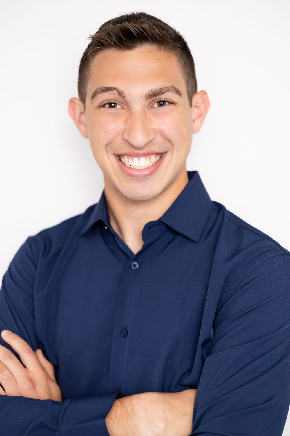 Young man in navy blue shirt smiling with arms crossed against white background.